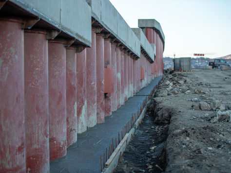 View of a construction site featuring large concrete columns, earthwork, and machinery.