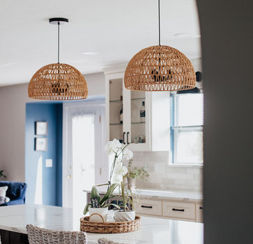 A large kitchen table with neutral-colored chairs and two hanging wicker lighting fixtures above it.
