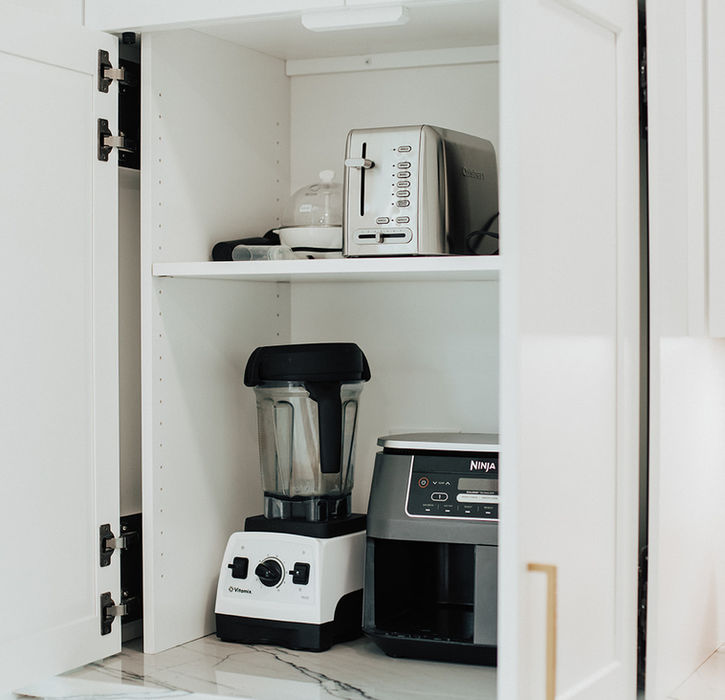 A cabinet opened in a kitchen to reveal small appliances.