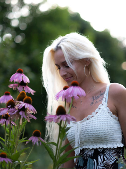 Nahaufnahme von Denise beim Betrachten rosa Blüten, verträumter Blick, sommerliche Natur, ruhige Momentaufnahme.