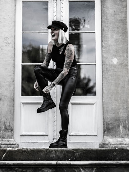 Ganzkörperportrait in Schwarz-Weiß: Natalie steht lachend auf der Schlosstreppe in Bad Salzuflen, beim Zubinden ihrer Boots, fotografiert von unten.
