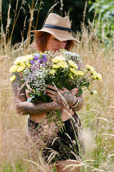 Verträumtes Porträt mit Blumenstrauß und Sommerhut, fotografiert im Grünen an der Heerser Mühle in Bad Salzuflen.