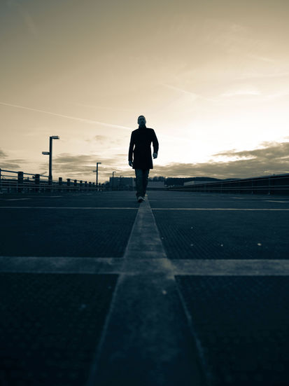 Silhouette eines Mannes bei Sonnenuntergang, schreitet auf Parkhaus-Markierungslinie Richtung Kamera, urbanes Portrait in Bielefeld.“