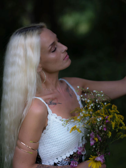 Denise mit Blumenstrauß, Augen geschlossen, lehnt an Ast im Garten der Heerser-Mühle – sinnliches Outdoor-Porträt bei natürlichem Licht.
