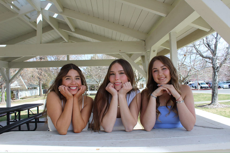 3 women leaning on a ledge, leaning their heads in their hands, smiling.