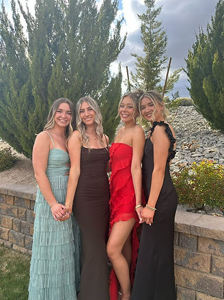 4 women in floor length dresses in front of trees, holding hands and smiling