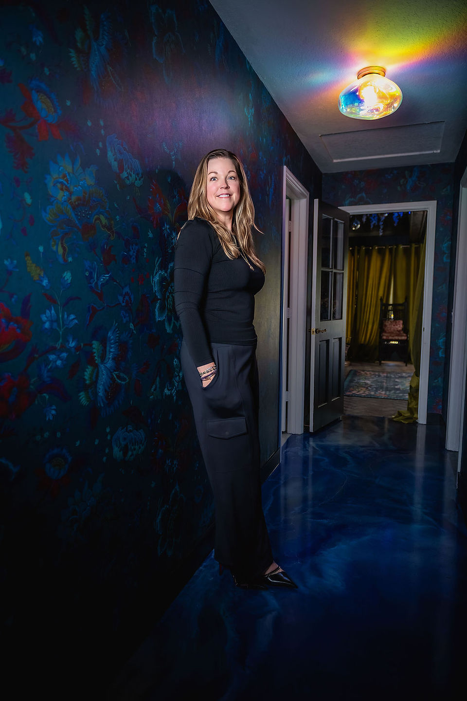 Woman entrepreneur stands in moody hallway with rainbow light fixture for personal branding shoot at Firefly Grove