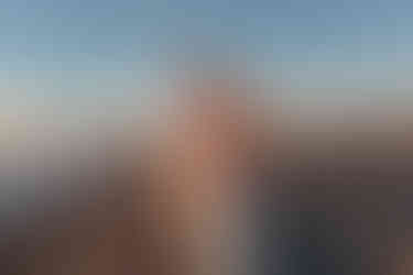 Couple standing on beach at sunset, man embracing woman from behind, both smiling