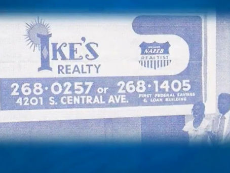 Blue-toned realty sign reading "Ike’s Realty" and NAREB logo with contact info and address. Two people stand on the right, partially visible.