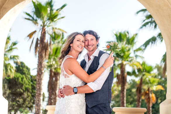 Bride and groom smiling and embracing under the historic Balboa Park archway during their intimate wedding ceremony with soft natural light