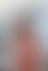 Couple embracing on a seaside boardwalk, woman in a pink dress holding her baby bump, smiles, ocean waves in the background.