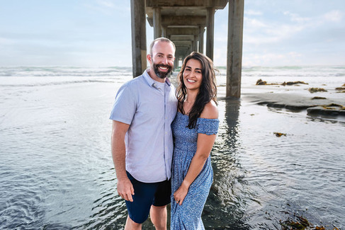 Husband and wife smiling together under Scripps Pier for family portraits in La Jolla, California