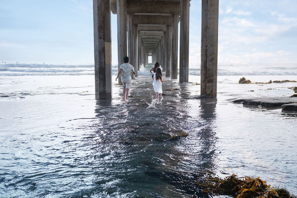 Three siblings running toward the ocean under Scripps Pier for a La Jolla beach family photography session