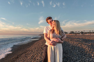 Man embracing woman from behind on beach at sunset with ocean in background