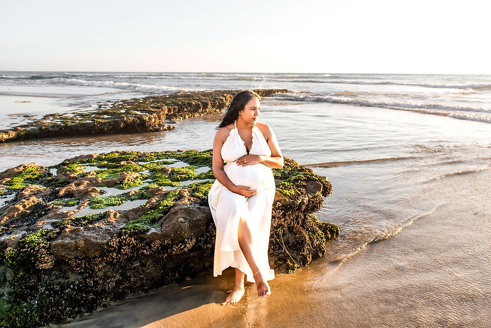 Elegant maternity portrait of a woman sitting barefoot on the sandy beach