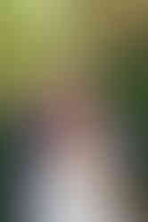 A man in a navy suit hugs a woman in a white dress outdoors, surrounded by lush greenery. Both appear happy and relaxed.