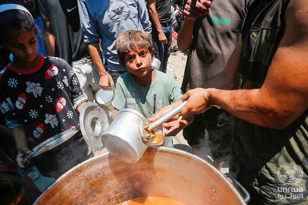 Archival photograph of displaced Palestinians receiving food in Deir al-Balah, Gaza, 26 June 2024. Ashraf Amra / UNRWA, CC BY-SA 3.0 IGO.