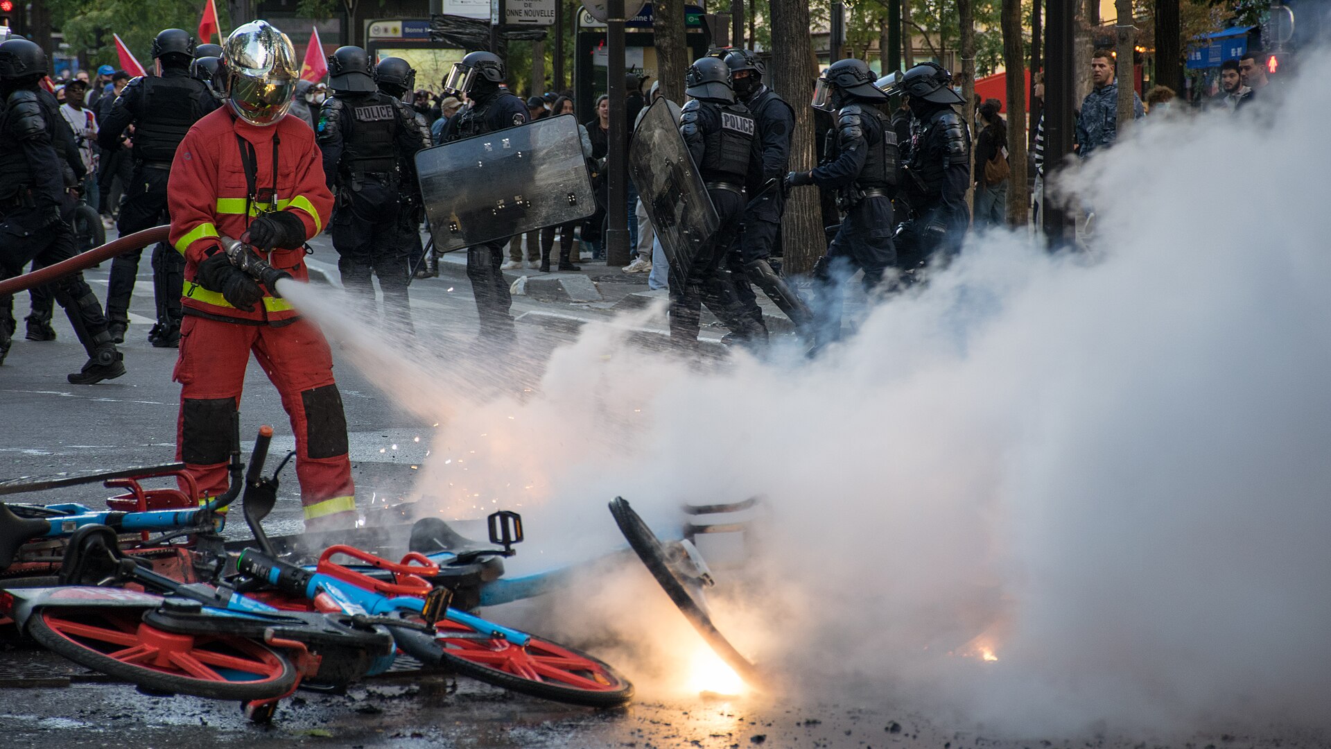 A firefighter extinguishes burning bicycles as riot police stand nearby during a Paris demonstration