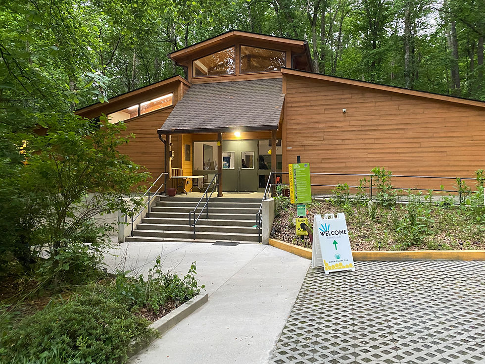 Wooden Outdoor Activity Center building with a sloped roof surrounded by trees, featuring a "Welcome" sign by the steps. The setting is peaceful and inviting.