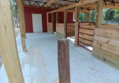 Red steel truss horse barn with enclosed feed room built in Dade City, FL by Patriot Pole Barns, used as a multi-purpose horse barn
