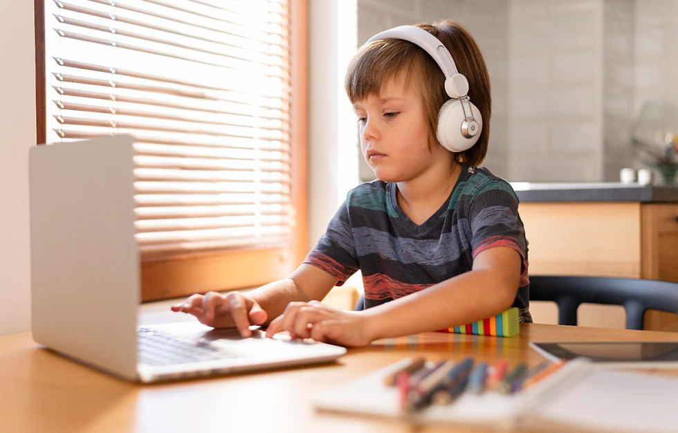 Child in striped shirt focused on laptop, wearing headphones at wooden desk. Sunlit room with blinds, colorful pencils nearby.