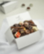 Geöffnete weiße Geschenkbox, gefüllt mit einer Auswahl an Pralinen und Schokoladen, verkaufsbereit.