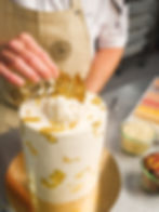 Handwerkliche Torte mit „Happy Birthday“-Dekoration, goldenen Details und weißen Zuckerrosen aus der Konditorei.
