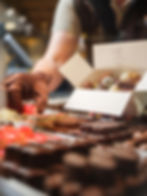 Ein Chocolatier mit Handschuhen legt Pralinen in eine weiße Geschenkbox an einer Theke.