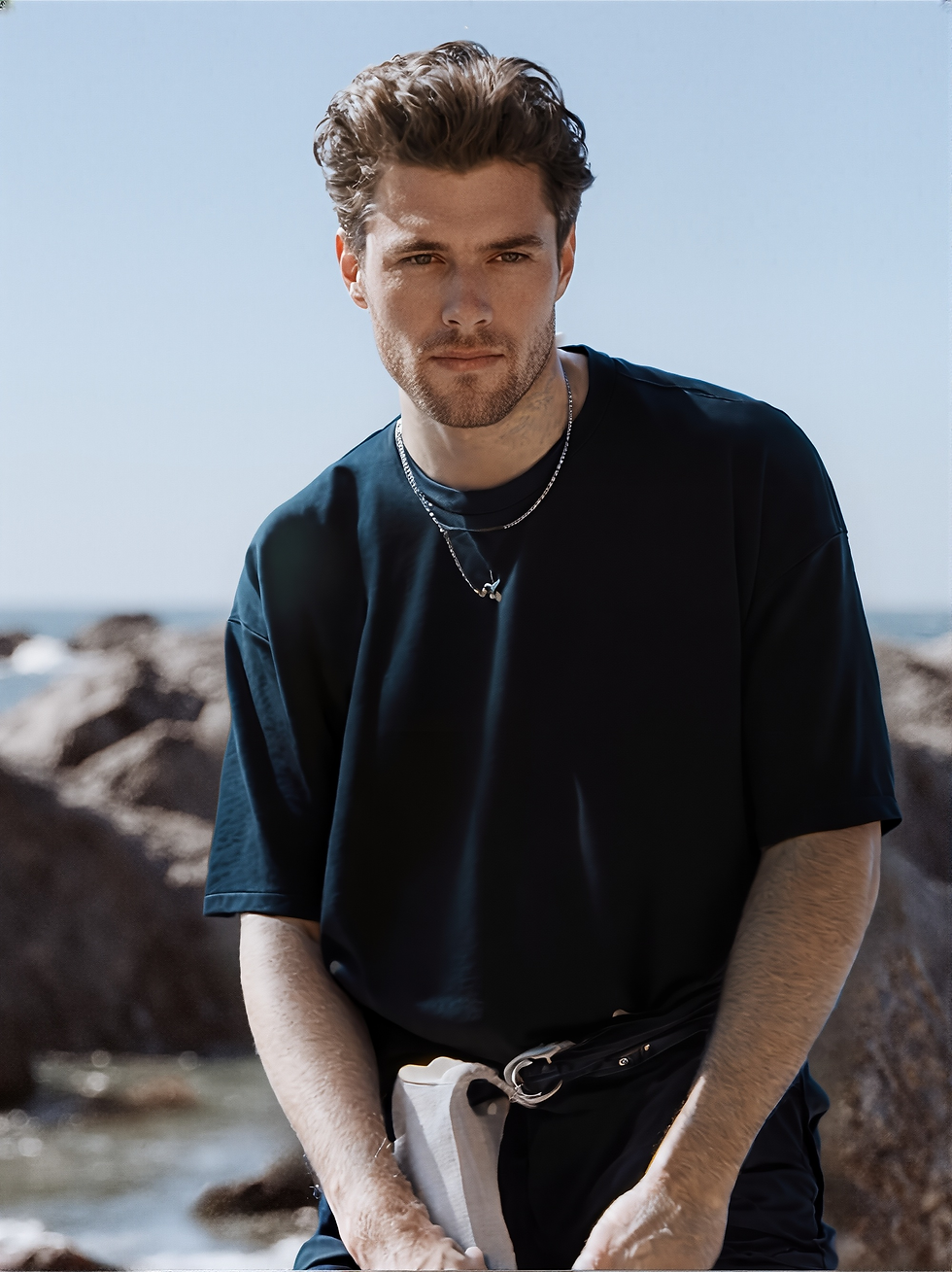 Thumbnail: Young man in navy blue terry oversized t-shirt posing on a rocky beach.