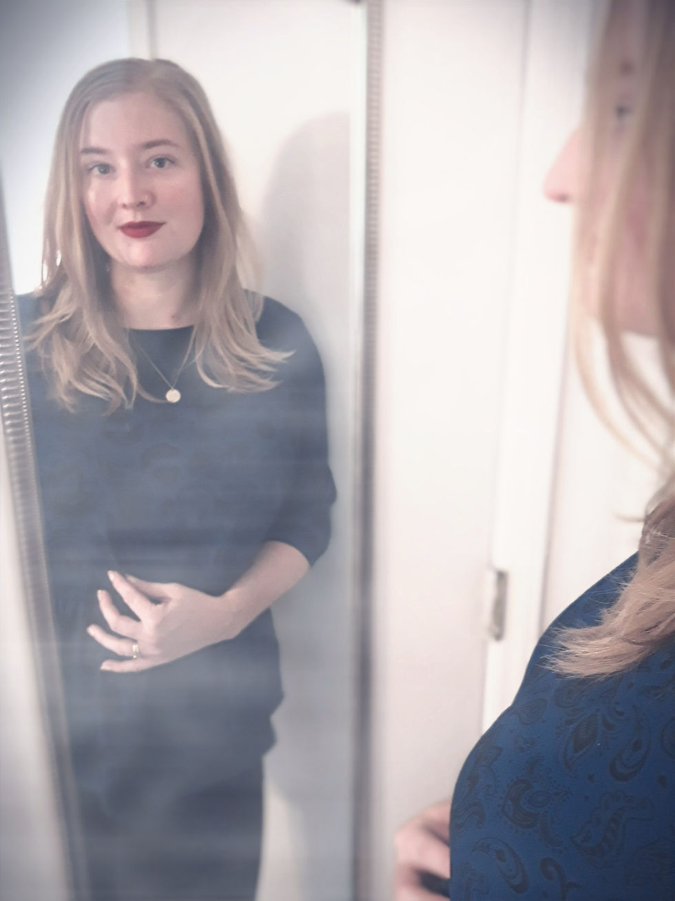 Alex looks in a mirror, we can see her reflection over her shoulder.