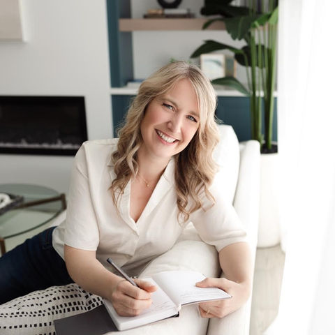 Smiling woman sitting on couch, writing in journal notebook.