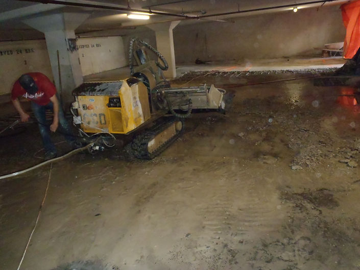 A man operates a machine in a garage, focused on his task amidst tools and equipment surrounding him