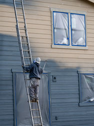A person on a ladder working on the siding of a house