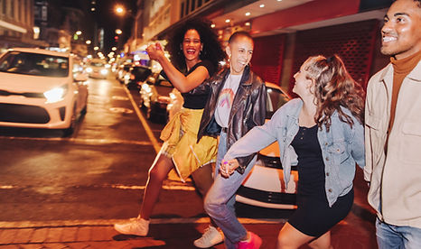 A joyful group of four friends walk hand in hand down a lively city street