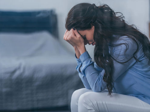Focus of woman sitting and covering face with hands in bedroom
