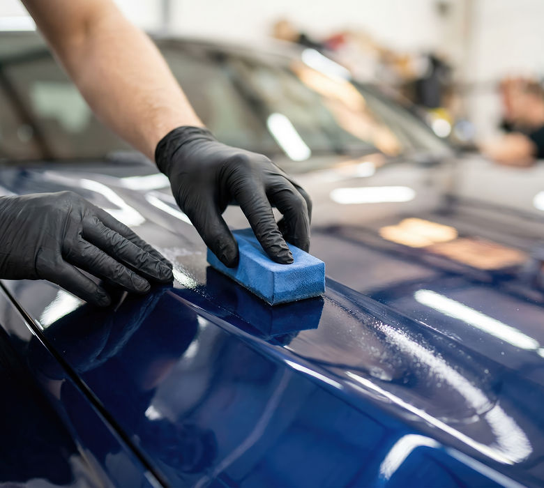 Car detailing specialist applying wax or ceramic coating to a blue car