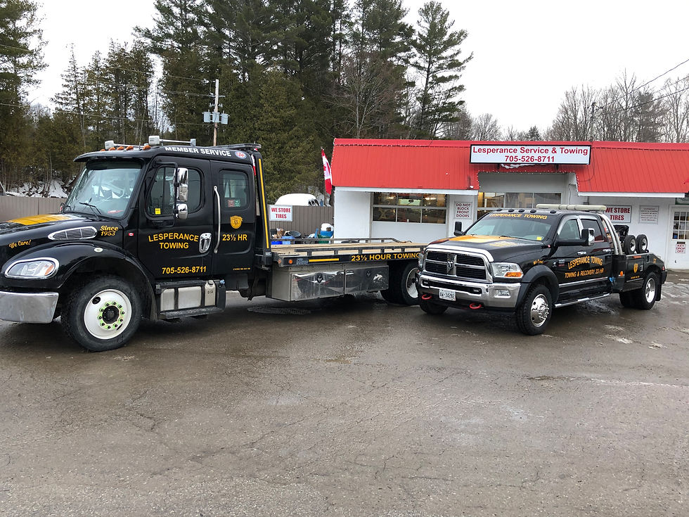 Two black tow trucks parked in front of Lesperance Service & Towing with a red roof and trees in the background.