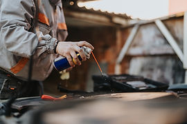 A technician wearing a work jacket sprays a liquid lubricant over the engin