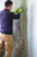 The man uses a spatula to remove mold and fungus on the wall