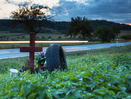 Lights of moving cars on a rural road near the place of a fatal accident where there is a wooden cross and truck tire