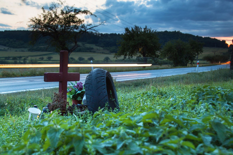 Lights of moving cars on a rural road near the place of a fatal accident where there is a wooden cross and truck tire