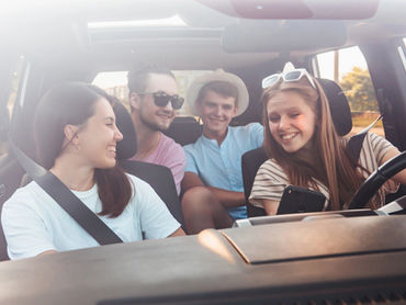 Four teenage friends in a car. Passenger is showing the driver something on her phone