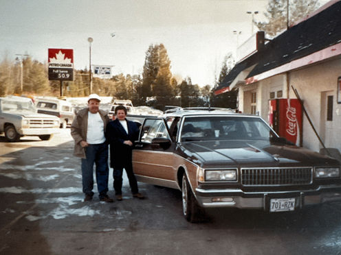 Vintage towing company owners standing beside classic sedan outdoors