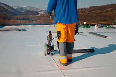 Un couvreur applique une membrane sur un toit plat.