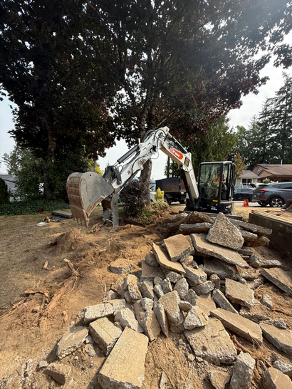 Excavator piling up broken concrete debris on dirt ground