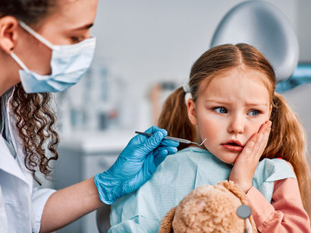 Little girl being examined by a dentist holding her cheek with a tooth ache