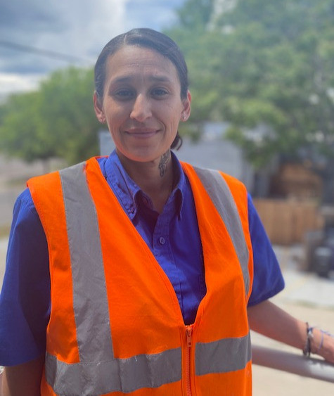 Woman in purple uniform and orange safety vest working outdoors in downtown Denver.