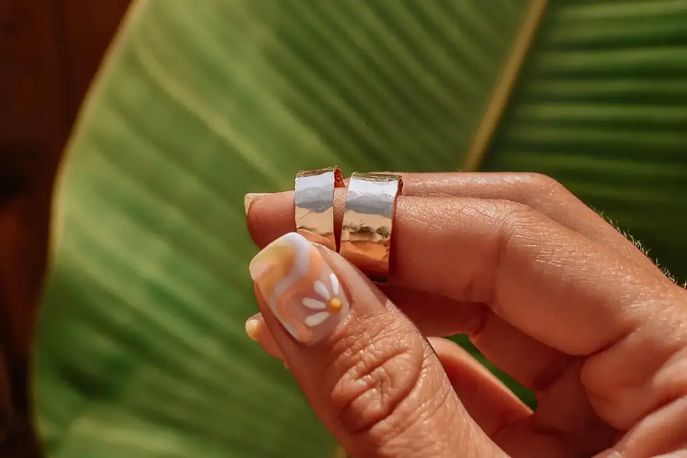 Hand holding two gold filled wide band rings in front of a tropical green leaf