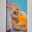 Miniaturbild: Frau in gelbem Plastikkleid lehnt sich an eine Kuh. Acrylbild auf Leinwand. Titel: „Beauty & the Beef“., seitlich
