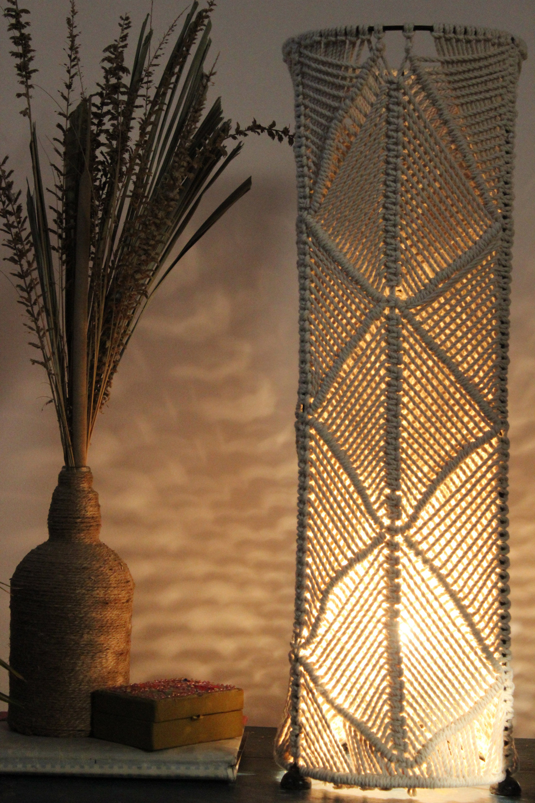 Boho macrame floor lamp with cotton yarn weaving, on metal frame, rustic and artistic lighting, lights on.